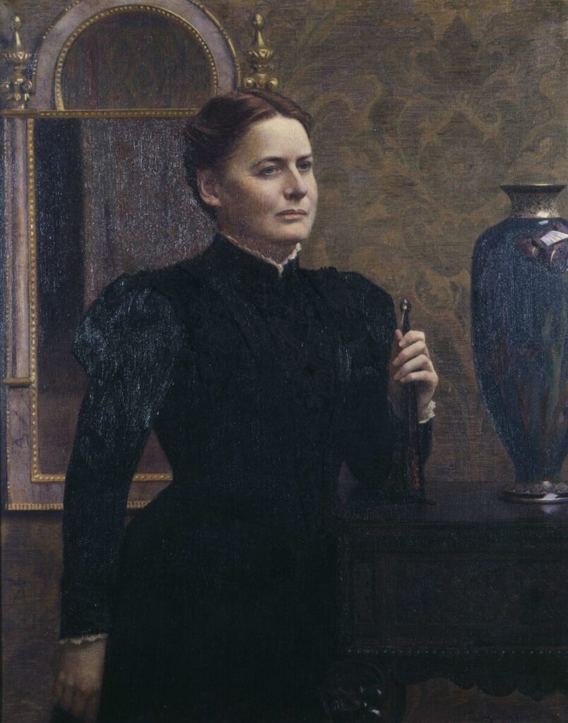 Portrait of Harriet Sarah Walker wearing a black dress and her hair pulled back, posed next to a blue vase with a mirror behind her.