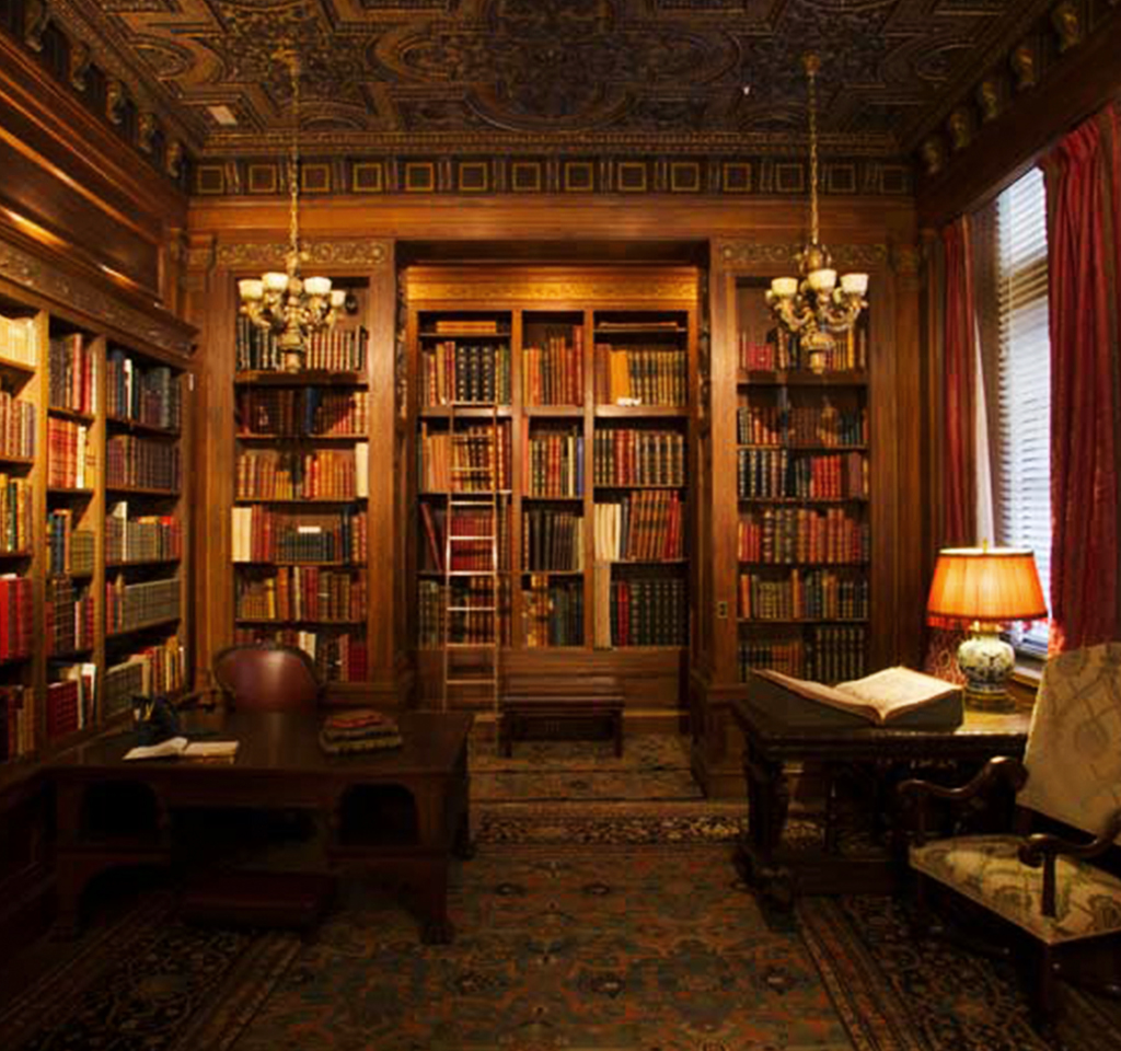 Interior photo of an intimate library room with chandeliers and an ornately carved ceiling.