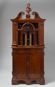 Alternate view of Mahogany cabinet with a glass panel revealing brass tubes and a carved bust on top.