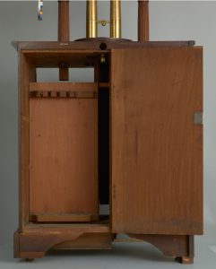 Alternate view of Mahogany cabinet with a glass panel revealing brass tubes and a carved bust on top.