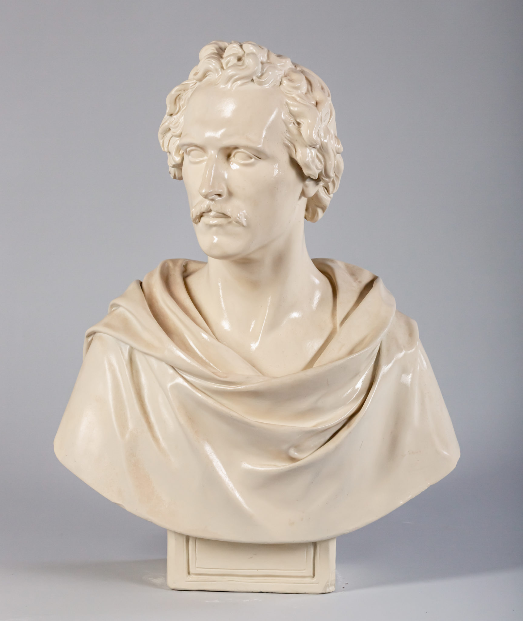Glazed ceramic bust of a man with short, curly hair and a mustache, draped in a toga.