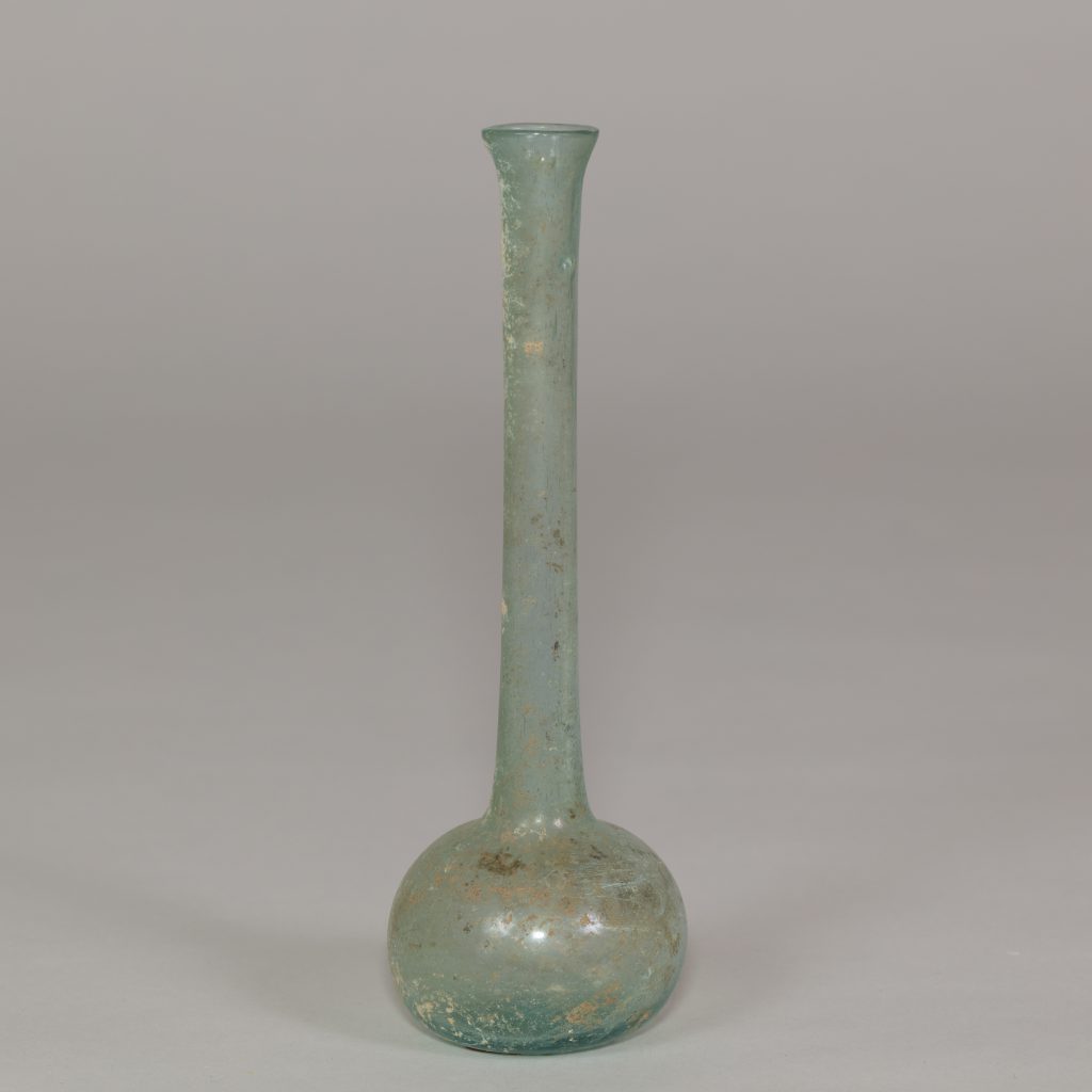 An ancient paritally-transparent glass vessel with a long narrow neck and a wider round base. It is tinted green with some brownish-gold flecks of worn paint.