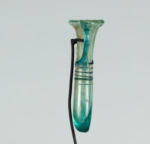 Alternate view of An ancient narrow, two-handled glass vessel tinted teal. The vessel is a long pipe shape folded in half so the two opening meet at the top.