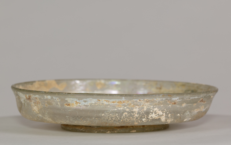 Alternate view of An ancient glass dish mostly transparent after brown and gold paint worn away.