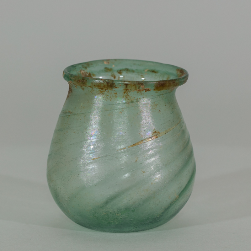 Alternate view of An ancient small, paritally-transparent glass jar tinted green with some brownish paint marks toward the lip.