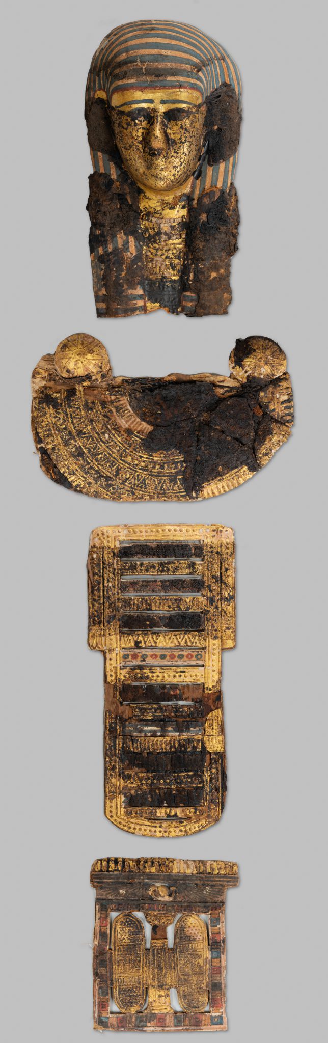 Four sculptural fragments including a mummy mask and three panels with intricate carvings and patterns in gold leaf.