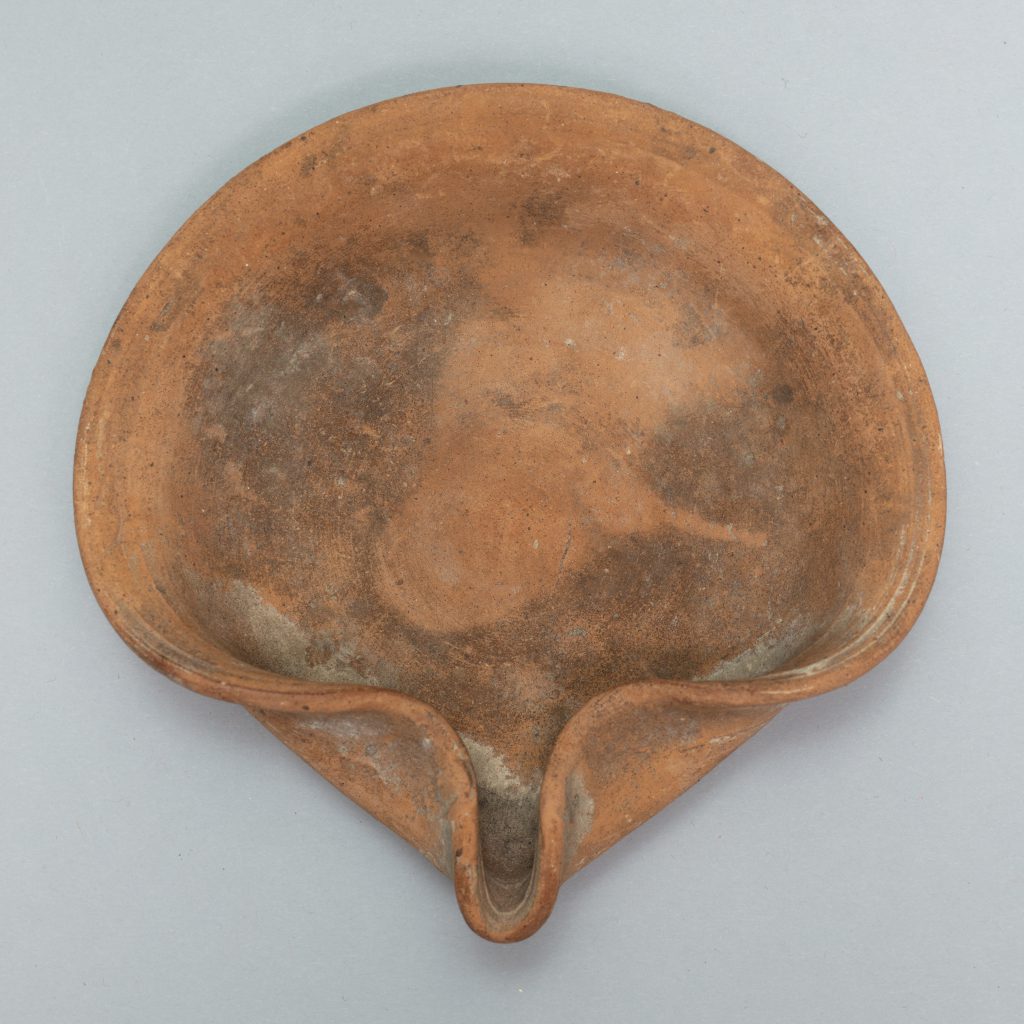 Circular terracotta lamp with one side of its lip folded into a curl.