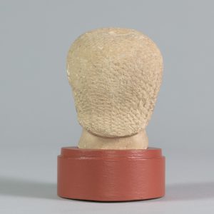 Alternate view of White limestone carved head with closed eyes, mounted on a circular platform.