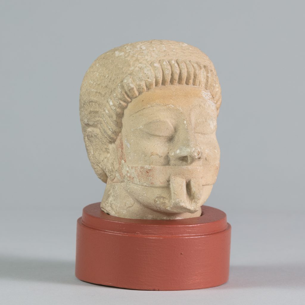 White limestone carved head with closed eyes, mounted on a circular platform.