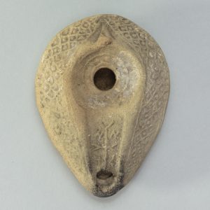 An overhead view of an ancient, whitish, ovular oil lamp.