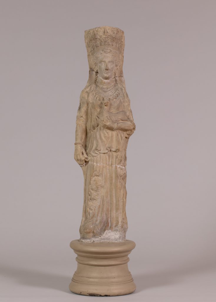 Alternate view of Terracotta statue of a goddess wearing a tall headdress and carrying a fawn, mounted on a circular stand.
