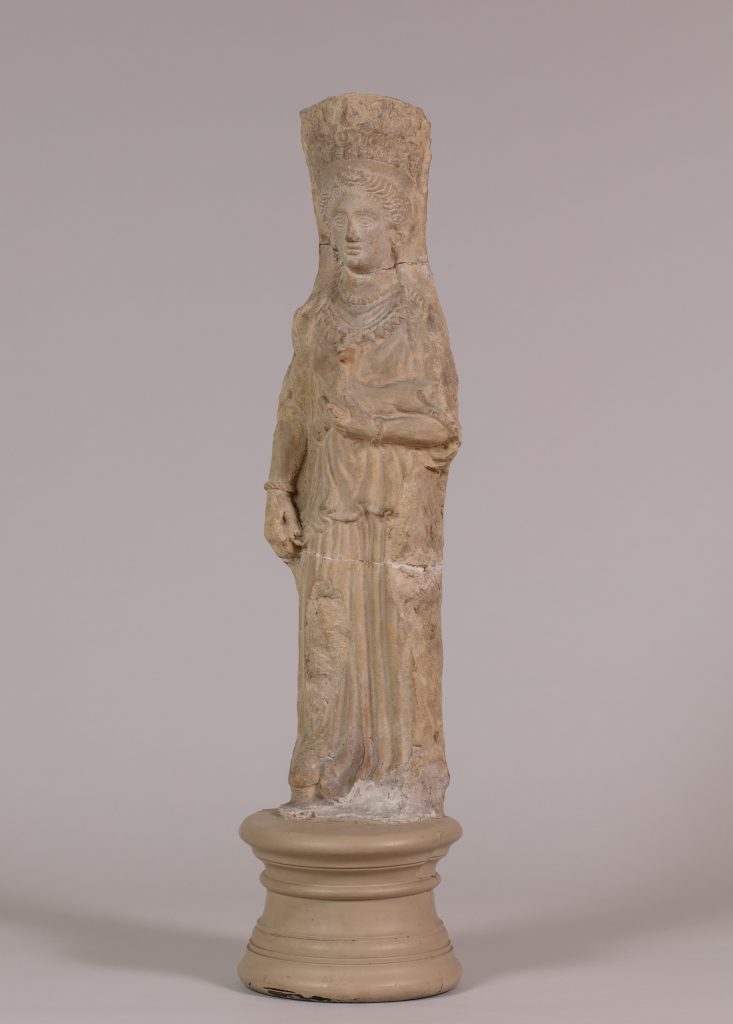 Terracotta statue of a goddess wearing a tall headdress and carrying a fawn, mounted on a circular stand.