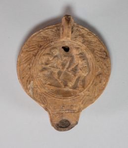 Circular terracotta lamp with relief carving of gladiators on its top.
