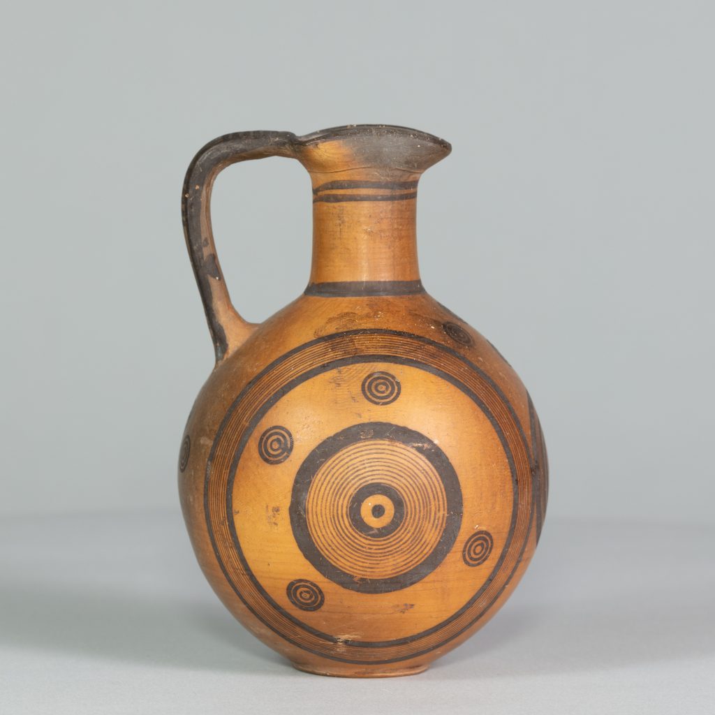 Orange terracotta jug with one handle and black circular patterns painted on its surface.