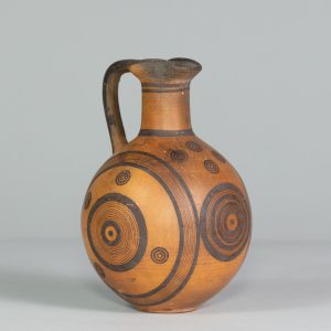 Alternate view of Orange terracotta jug with one handle and black circular patterns painted on its surface.