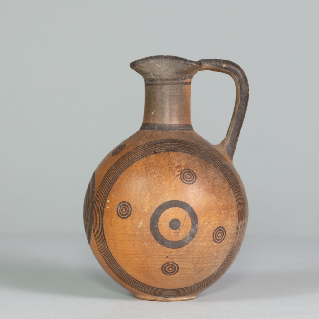 Alternate view of Orange terracotta jug with one handle and black circular patterns painted on its surface.