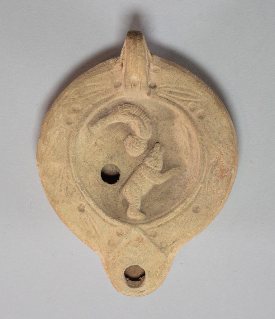 Circular terracotta lamp with with bear and person carved into its surface.