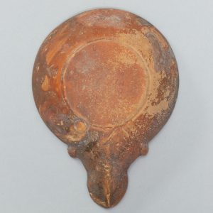 Alternate view of Circular terracotta lamp with gladiatorial weapons carved in a circle on its surface.