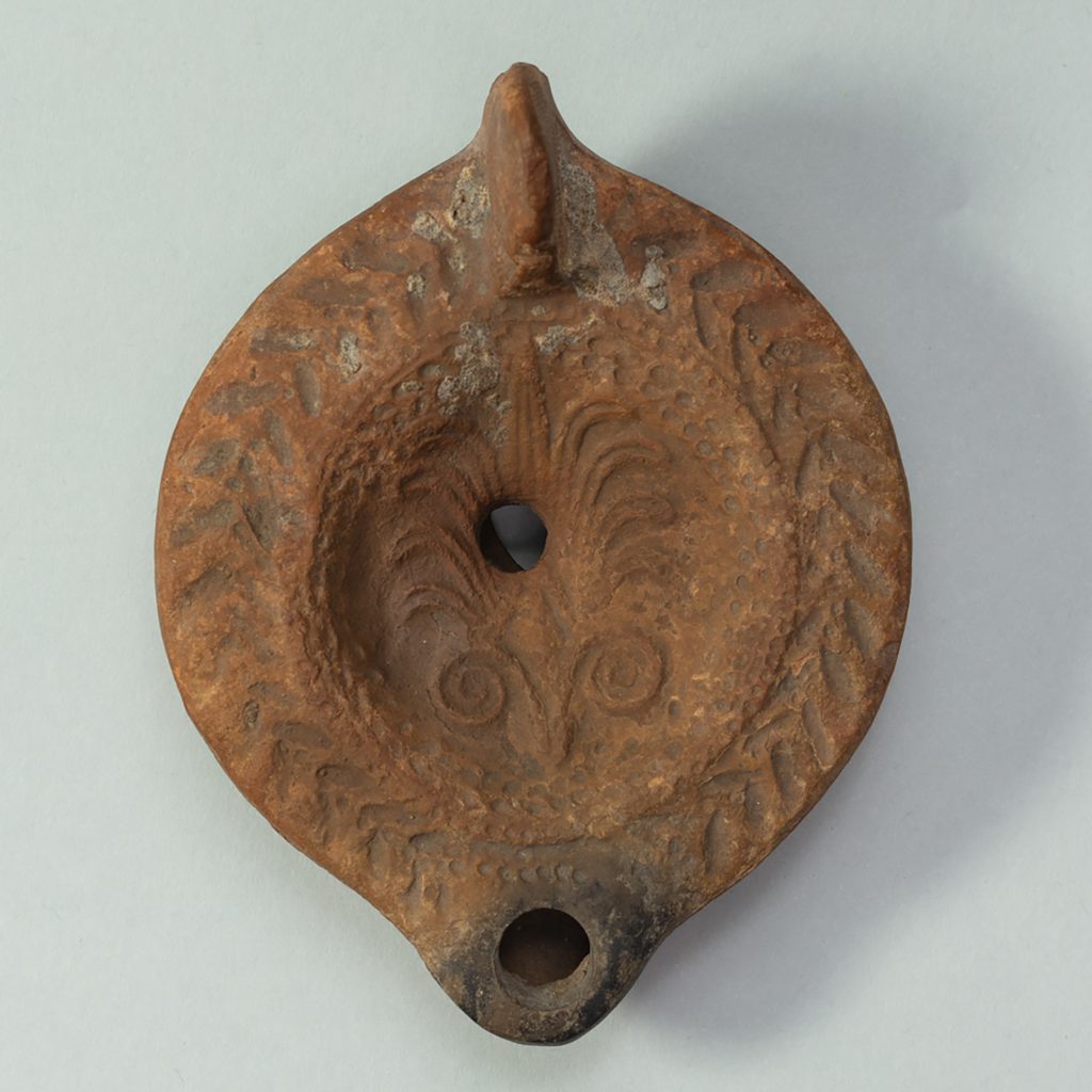 Circular terracotta lamp with palmette pattern carved into its surface.