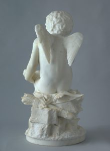 Alternate view of White marble statue of a winged cupid sitting atop a decorative pedestal and looking thoughtfully into the distance.