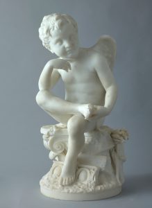 White marble statue of a winged cupid sitting atop a decorative pedestal and looking thoughtfully into the distance.