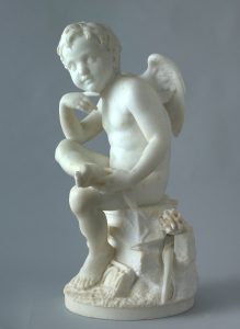 Alternate view of White marble statue of a winged cupid sitting atop a decorative pedestal and looking thoughtfully into the distance.