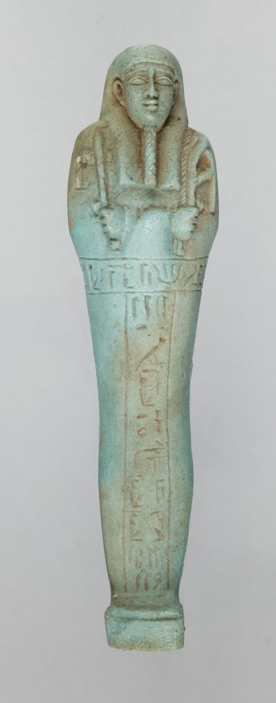 A bluish-green tinted ancient Egyptian figurine careved into the form of a mummy. It has a narrow beard, closed eyes, and folded arms.