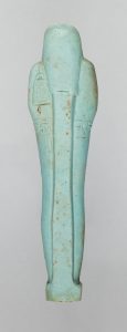 Alternate view of A bluish-green tinted ancient Egyptian figurine careved into the form of a mummy. It has a narrow beard, closed eyes, and folded arms.
