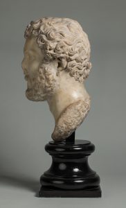 Alternate view of White marble portrait head of a man with short curly hair and a beard, mounted on a black base. The nose is partially broken off.