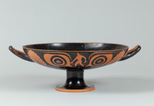 Wide, low terracotta cup with two handles, painted with red figures, scalloped shells, and other designs.