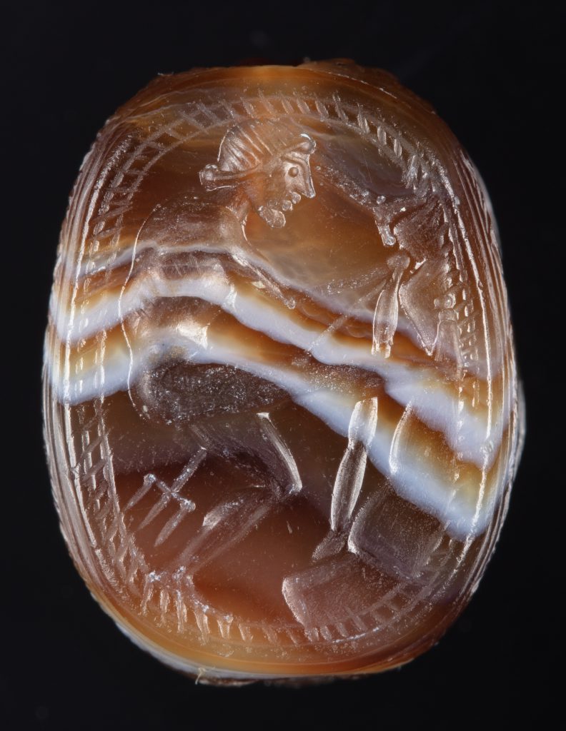 Onyx, scarab-shaped cameo depicting Poseidon pulling his trident from a rock. A white stripe curves across the amber-colored surface.