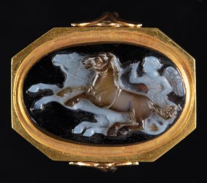 Gold-framed onyx cameo depicting a person riding a two-horse chariot.