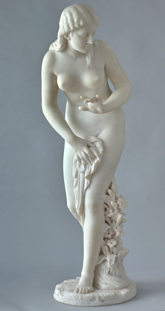 White marble statue of a nude young woman partially covering her bottom half with a sheet, flowers climbing up her left leg.