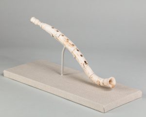Ivory flute resembling a modern recorder, mounted on a small base.