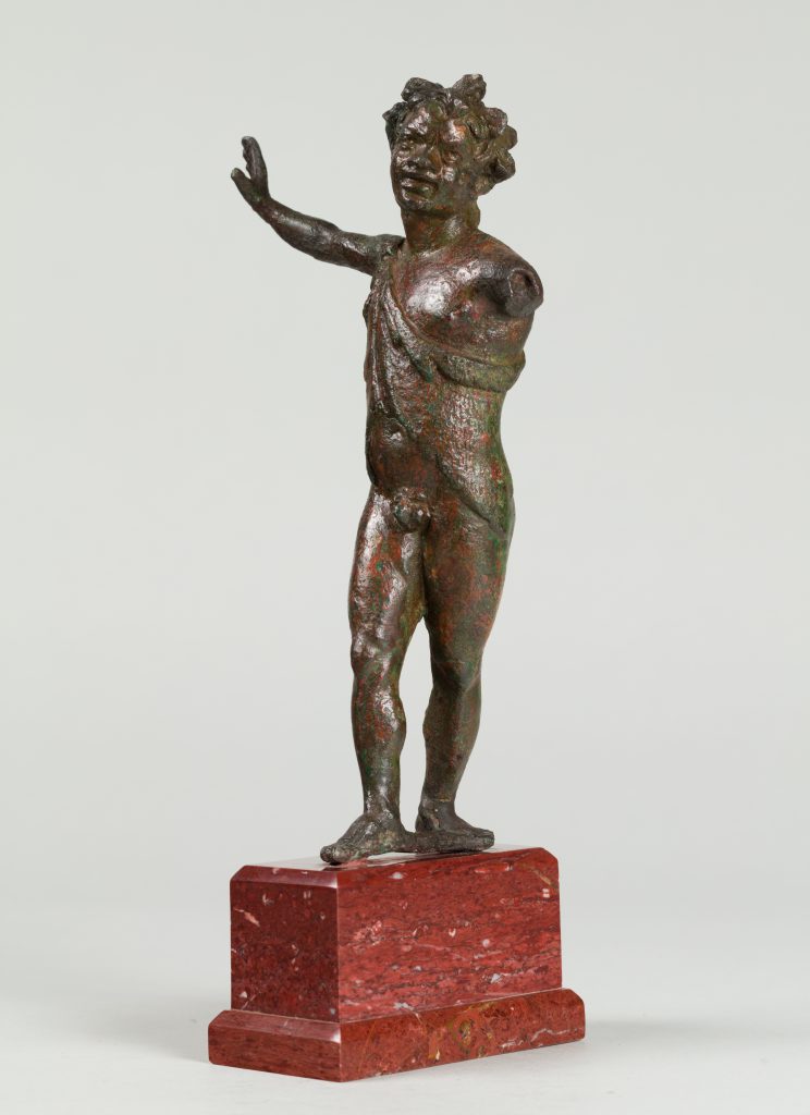 Small bronze statue of a dancing satyr with one arm extended and the other arm missing. Mounted on a wooden base.