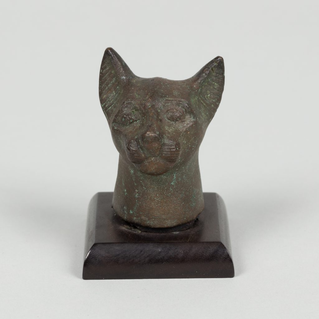 Bronze sculpture of a cat head mounted on a wooden base.