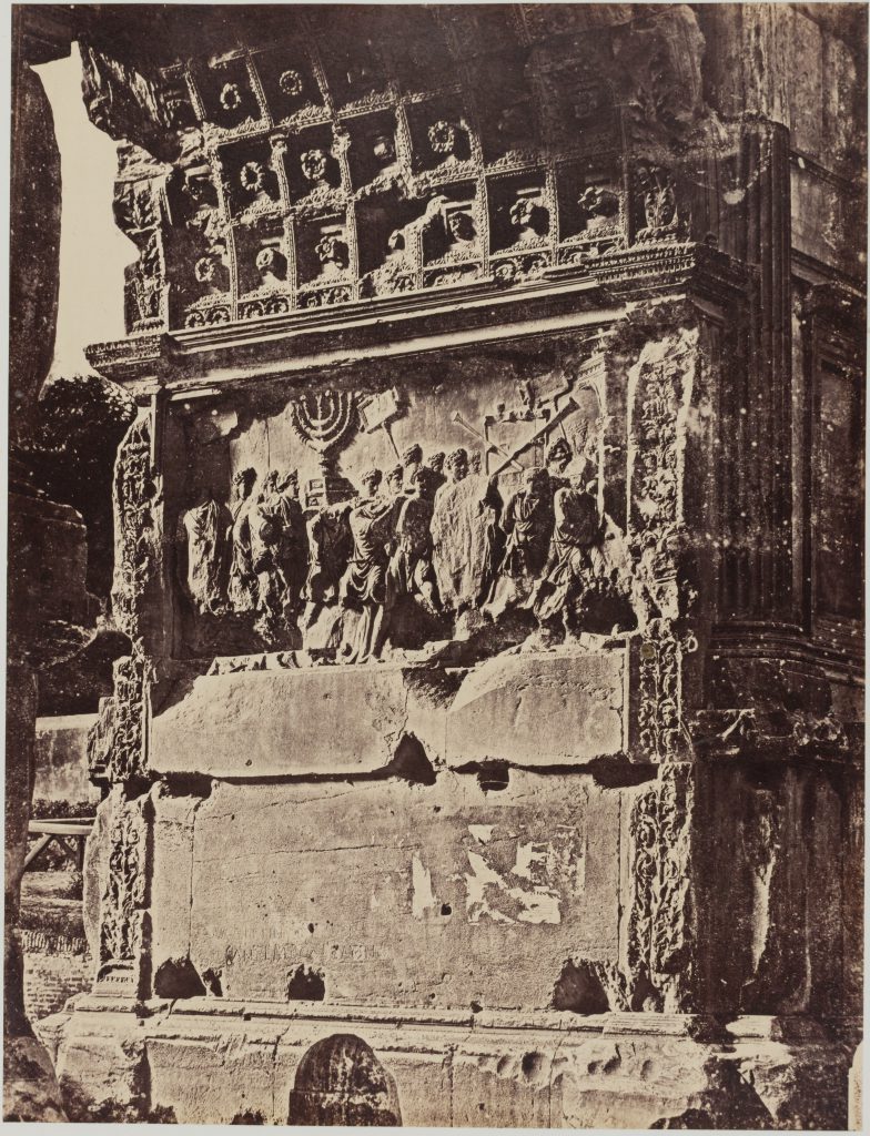 Black and white photograph of a detail on the Arch of Titus, featuring several carved figures engaged in battle.