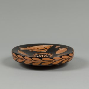 A thick ceramic plate decorated with red fish, squid, clam shells, and floral pattern on a black background.