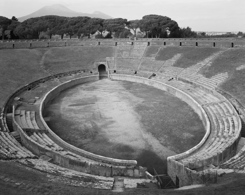 Black and white photo of an aerial view of the ovular amphetheater with trees and mountains in the background.