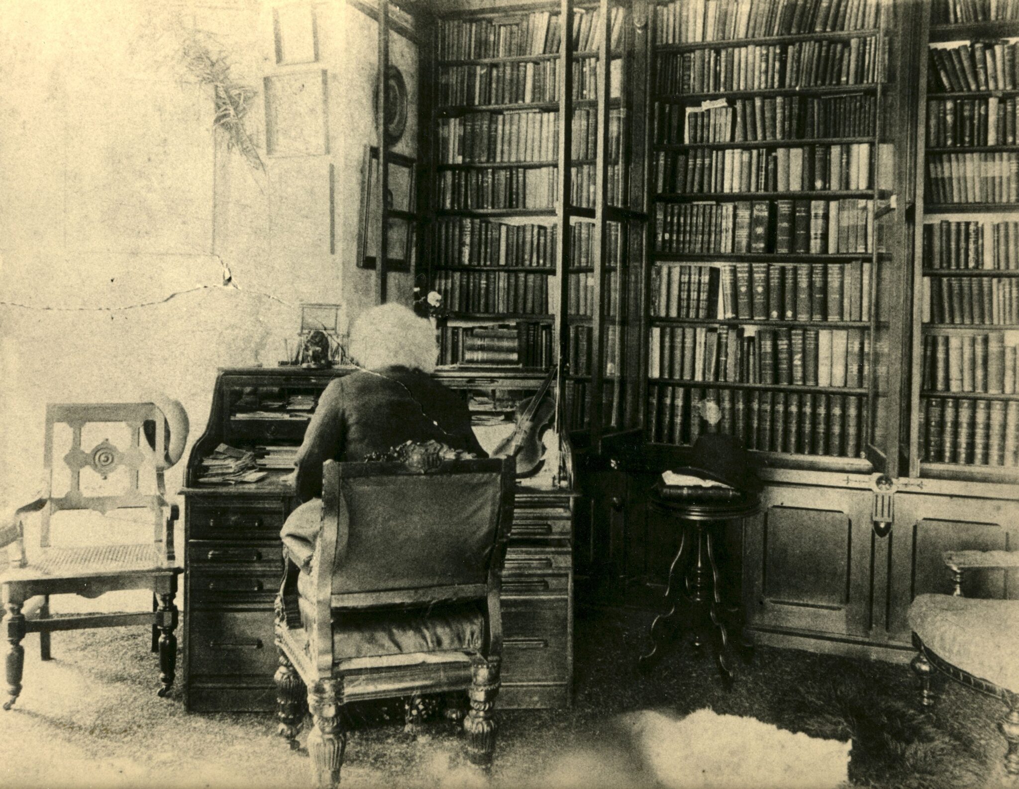 Sepia toned photograph of a man with white hair sitting at a desk in a library.