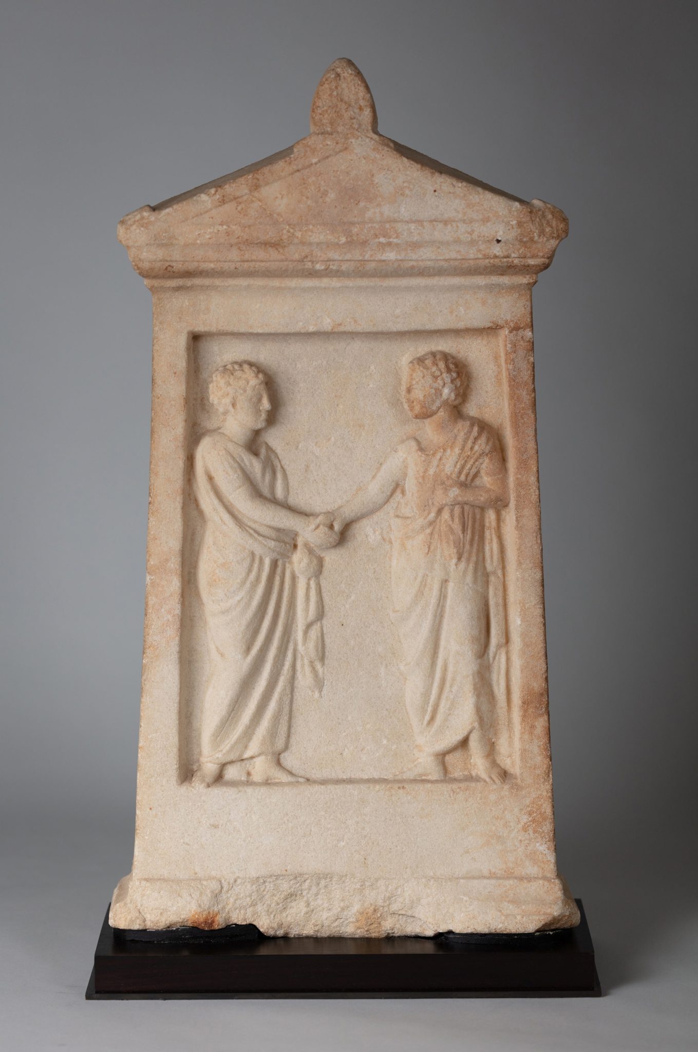 Ancient grave marker with a relief carving of two figures in togas, grasping hands.